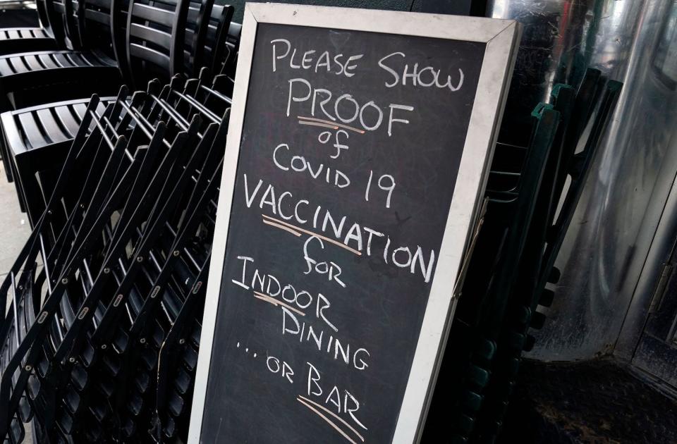 a sandwich board outside a restaurant reads: please show PROOF of COVID-19 vaccination for indoor dining or bar