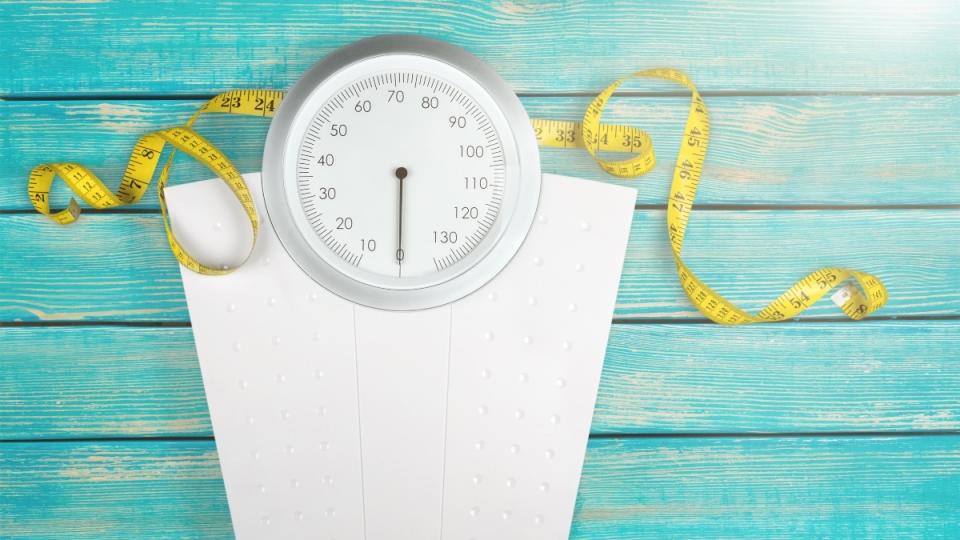 A white scale with a yellow measuring tape on blue floorboards