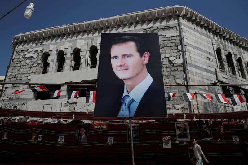 FILE PHOTO: FILE PHOTO: A man walks past a banner depicting Syrian president Bashar al-Assad in Douma