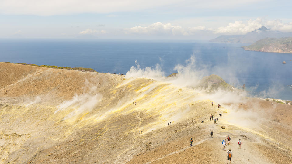 people walking on the edge of the crater. Mt. Etna in far distance