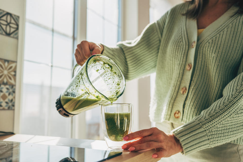 Person pouring green smoothie from blender into glass, promoting healthy eating