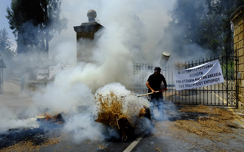 A farmer tries to control burning bales of hay outside the entrance gates, marked with a sign, of Cyprus's presidential palace