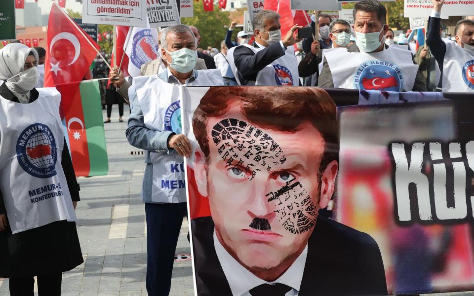 Men hold a sign bearing a picture of French President Emmanuel Macron with a shoe print on it as Turkish protesters shout slogans in Ankara, Turkey - ADEM ALTAN/ AFP