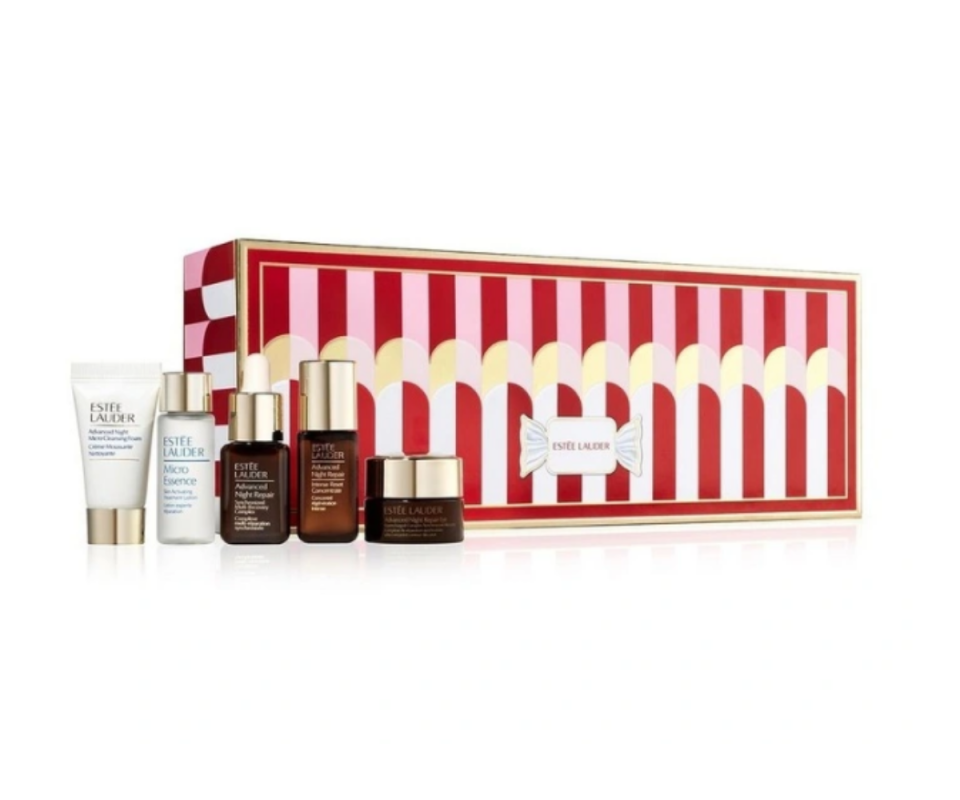 A long rectangular red and white striped box stands on a white background with five small skincare pots and serums in white and brown glass. 