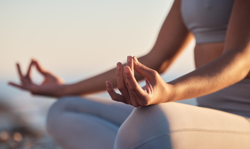 A person meditating, as they sit with their legs crossed and their hands resting on both knees. (Photo via Getty Images)