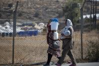 Migrants carry goods as they walk outside the new temporary refugee camp in Kara Tepe, near Mytilene the capital of the northeastern island of Lesbos, Greece, Thursday, Sept. 17, 2020. Greek police are moving hundreds of migrants to an army-built camp on the island of Lesbos Thursday after a fire destroyed an overcrowded facility, leaving them homeless for days. (AP Photo/Petros Giannakouris)