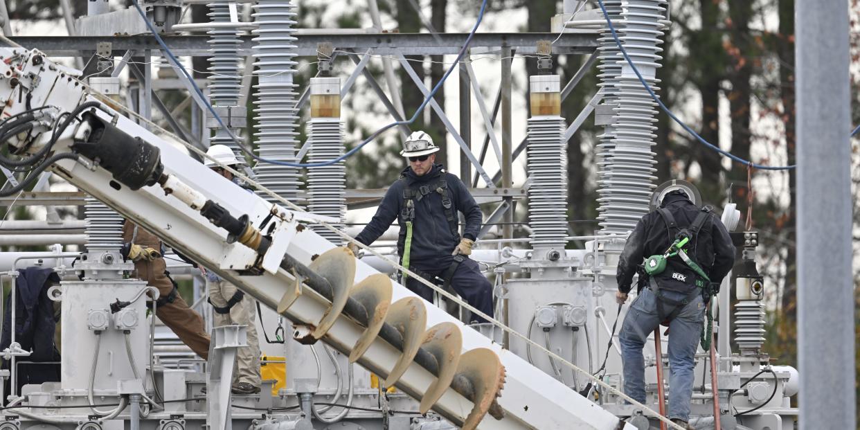 Workers stand amid electrical infrastructure.