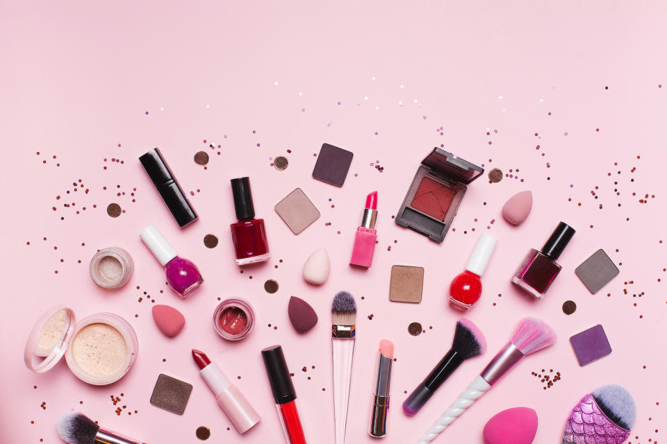 Top view of set of assorted tools and products for makeup application placed near shiny glitter on pink background