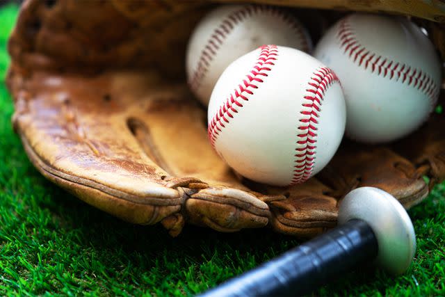 <p>Getty</p> A baseball glove with baseballs inside it and a baseball bat nearby (Stock Image).