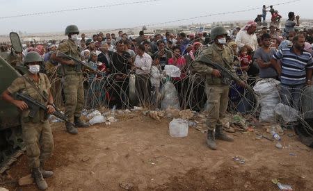 Turkish soldiers stand guard as Syrian Kurdish refugees wait behind the border fences to cross into Turkey near the southeastern town of Suruc in Sanliurfa province September 27, 2014. REUTERS/Murad Sezer