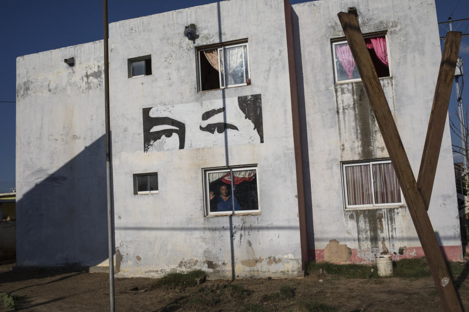 Nolberto Ortega, president of the Council of Communal Residences Villa de Dios, poses for a portrait from behind the window of his apartment, which the government gave him as part of a program coined Mission Housing and features the eyes of former President Hugo Chavez in Cabimas, near Maracaibo, Venezuela, Nov. 26, 2019. For many in Maracaibo, Venezuela's economic crash in the last five years hit especially hard. Once a center of the nation's vast oil wealth, production under two decades of socialist rule has plummeted to a fraction of its high, taking down with it residents' standard of living. (AP Photo/Rodrigo Abd)