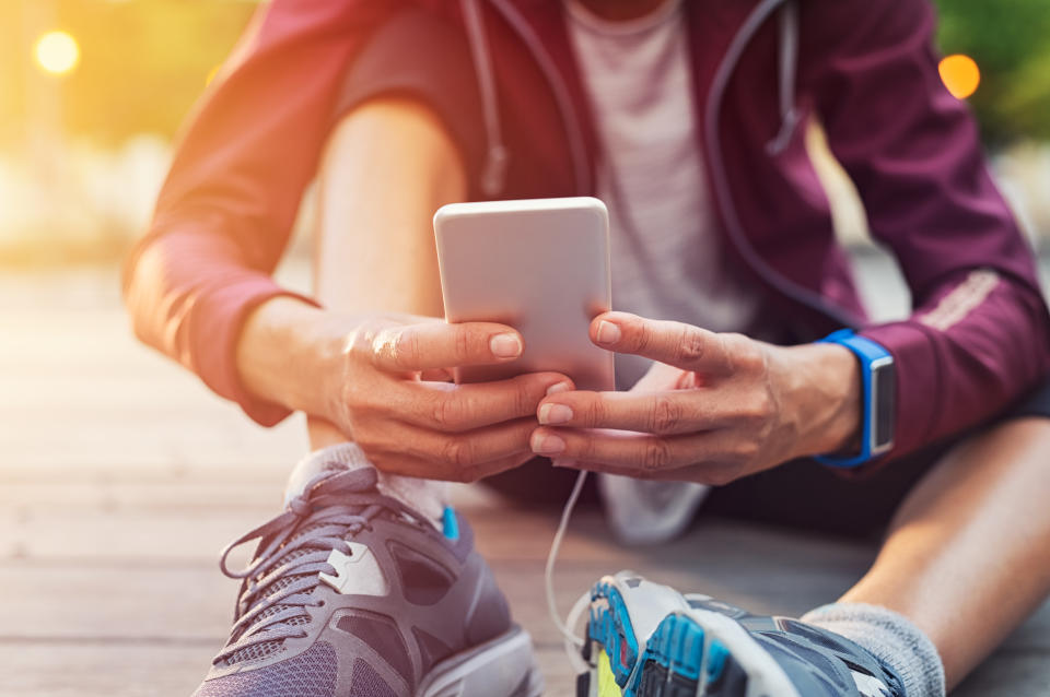 Closeup sporty woman hand using smartphone while sitting on floor. Woman wearing jacket and typing on mobile phone to check pulse rate in the early morning. Runner hand using smart phone while sitting on ground after running. (Getty Images)