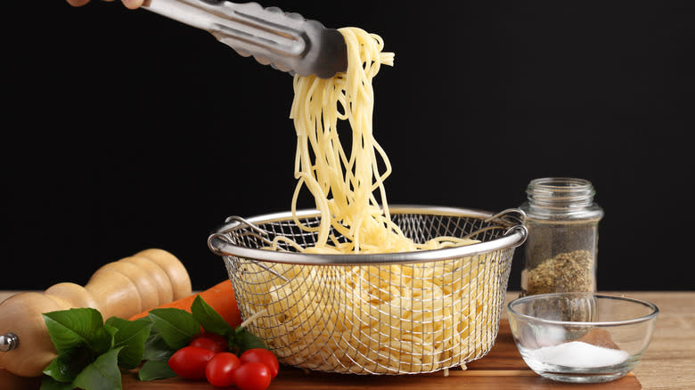 tongs holding spaghetti over strainer