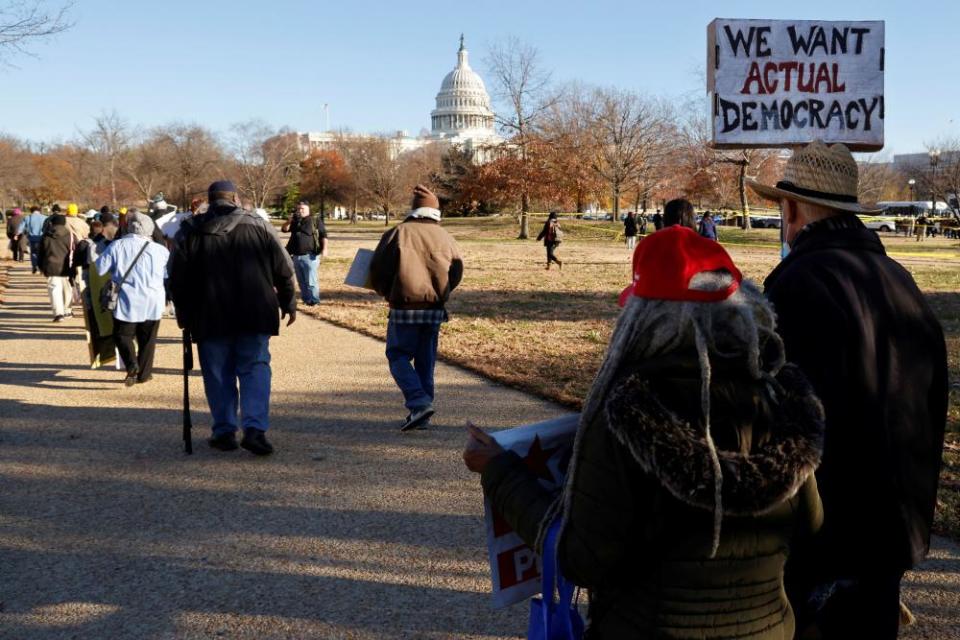 People walk towards the US Capitol, one of them holding a sign that says, 