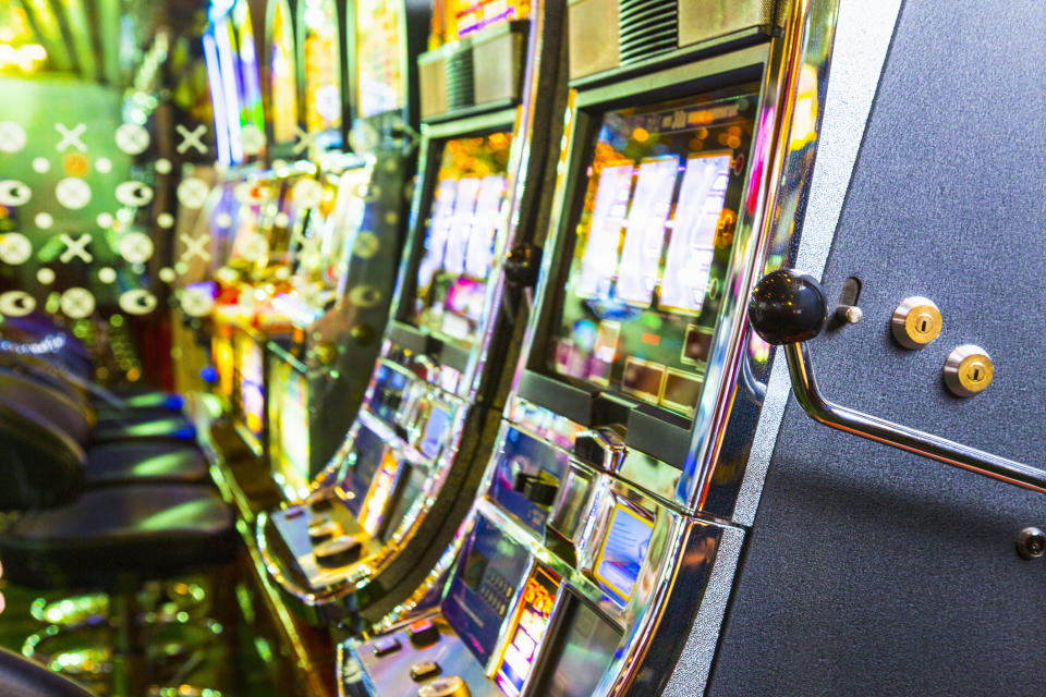 Rows of slot machines with bright lights and levers in a casino. No persons in the image