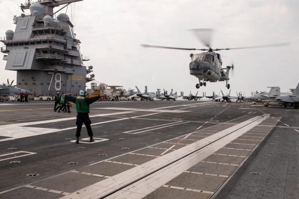 a helicopter lands on the flight deck of a military ship