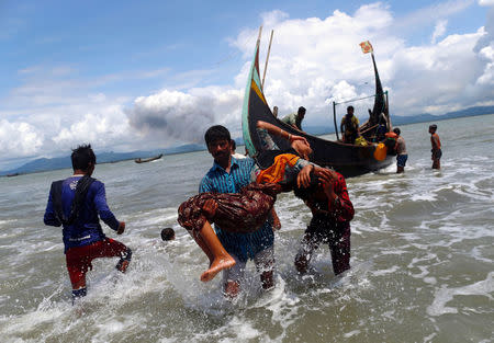 Smoke is seen on Myanmar's side of border as an exhausted Rohingya refugee woman is carried to the shore after crossing the Bangladesh-Myanmar border by boat through the Bay of Bengal, in Shah Porir Dwip, Bangladesh September 11, 2017. REUTERS/Danish Siddiqui