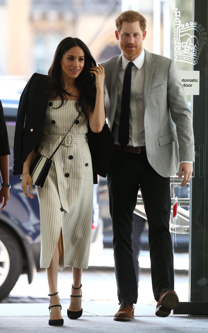 Meghan in a pinstripe cream dress with buttons and a jacket on her shoulders and Harry in a light grey suit jacket and dark pants and tie.
