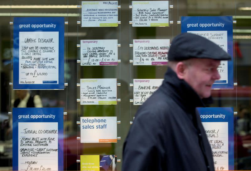 FILE PHOTO: A man walks past job advertisements in the window of a recruitment office in central London