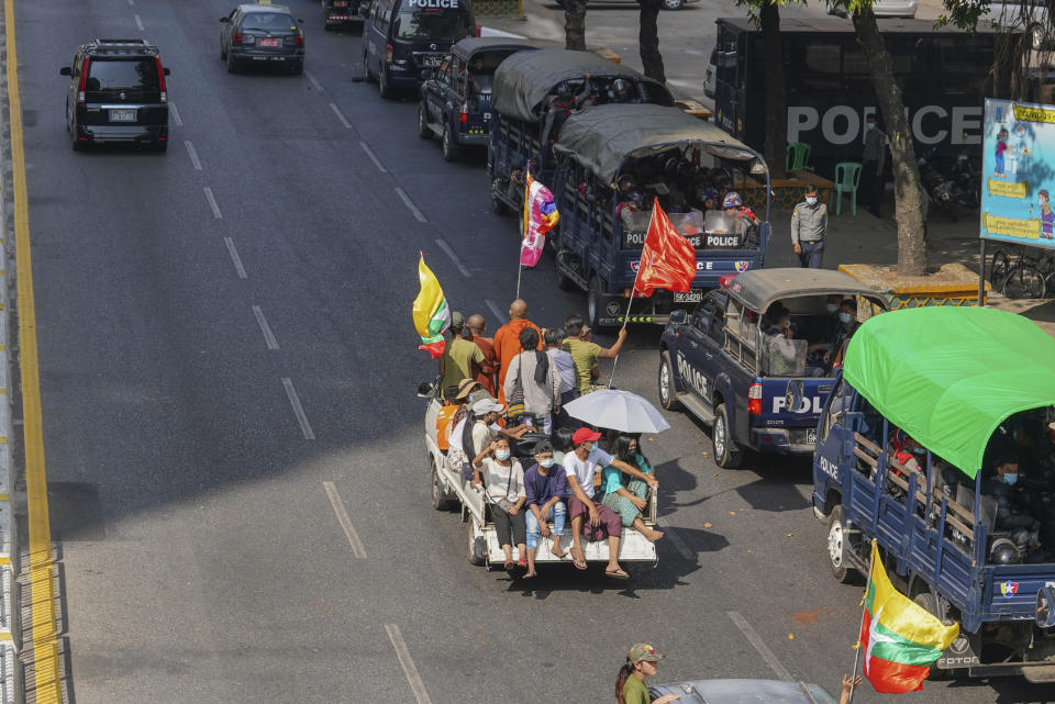 A vehicle with Myanmar and military flags and supporters of the Myanmar military and the military-backed Union Solidarity and Development Party passes by a row of police trucks with police security onboard parked near the Kyauktada police station in Yangon, Myanmar Monday, Feb. 1, 2021. Myanmar military television said Monday that the military was taking control of the country for one year, while reports said many of the country's senior politicians including Aung San Suu Kyi had been detained. (AP Photo)