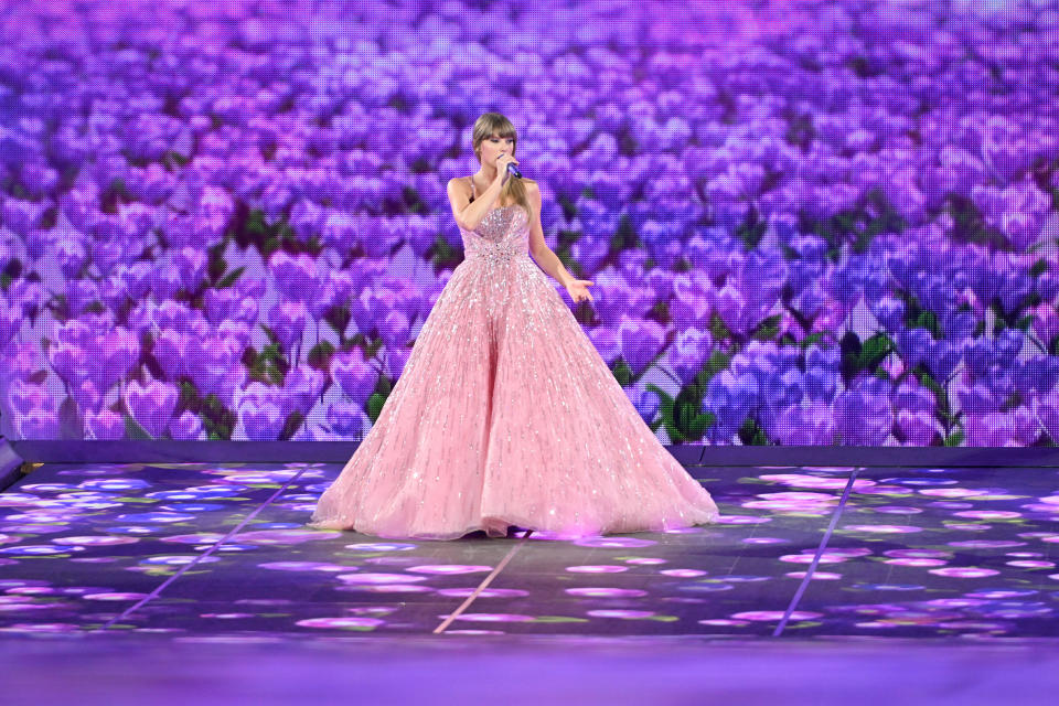 Taylor Swift in a pink gown with a purple backdrop during The Eras Tour