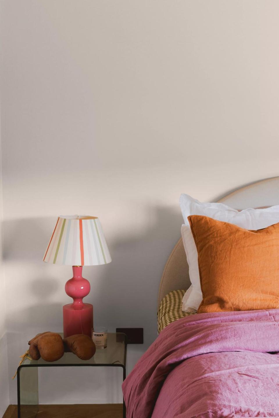 a lamp on a table next to a bed with colourful bedding and an off white pink on the walls