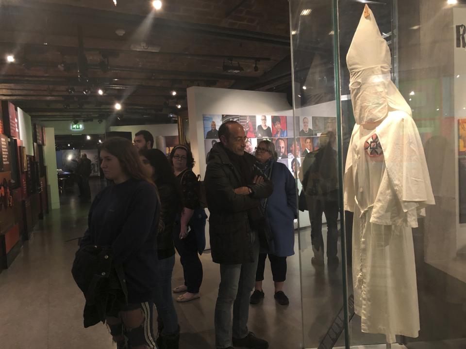 In this Nov. 24, 2019 photo, visitors at the International Slavery Museum in Liverpool, England, examine a display of a 1920s-era Ku Klux Klan outfit from Port Jervis, N.Y. The museum seeks to tell the story of the enslavement of people from Africa and how the British city benefited from human bondage. (AP Photo/Russell Contreras)