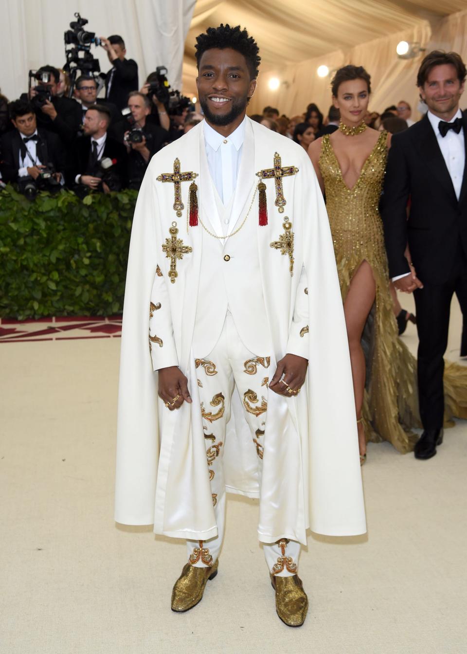 Chadwick Boseman arrives at the Met Gala wearing a white suit and cape adorned with gold crosses.