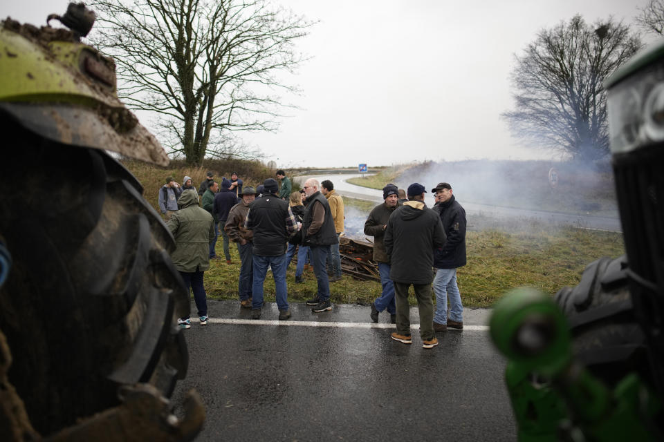 Farmers talk by a bonfire a they block a highway leading to Paris, Friday, Jan. 26, 2024 in Saclay, south of Paris. Snowballing protests by French farmers crept closer to Paris with tractors driving in convoys and blocking roads in many regions of the country to ratchet up pressure for government measures to protect the influential agricultural sector from foreign competition, red tape, rising costs and poverty-levels of pay for the worst-off producers. (AP Photo/Christophe Ena)