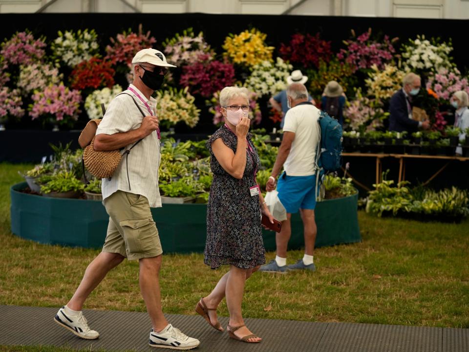 man woman walk past flower garden wearing masks