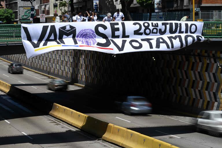 Estudiantes cuelgan un cartel que llama a votar por el candidato opositor Edmundo González Urrutia, en Caracas. (Federico PARRA / AFP)