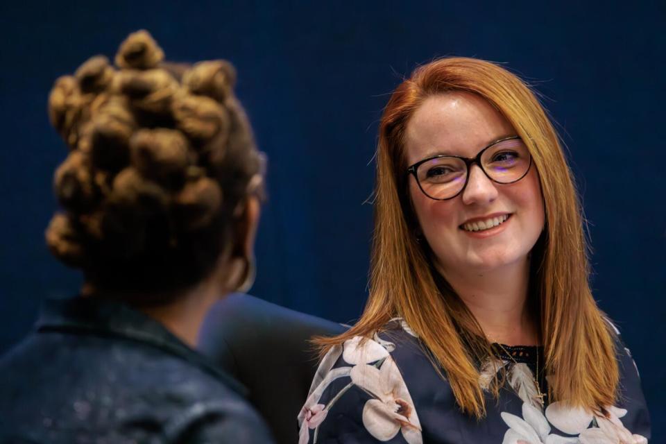 A smiling woman faces another woman.