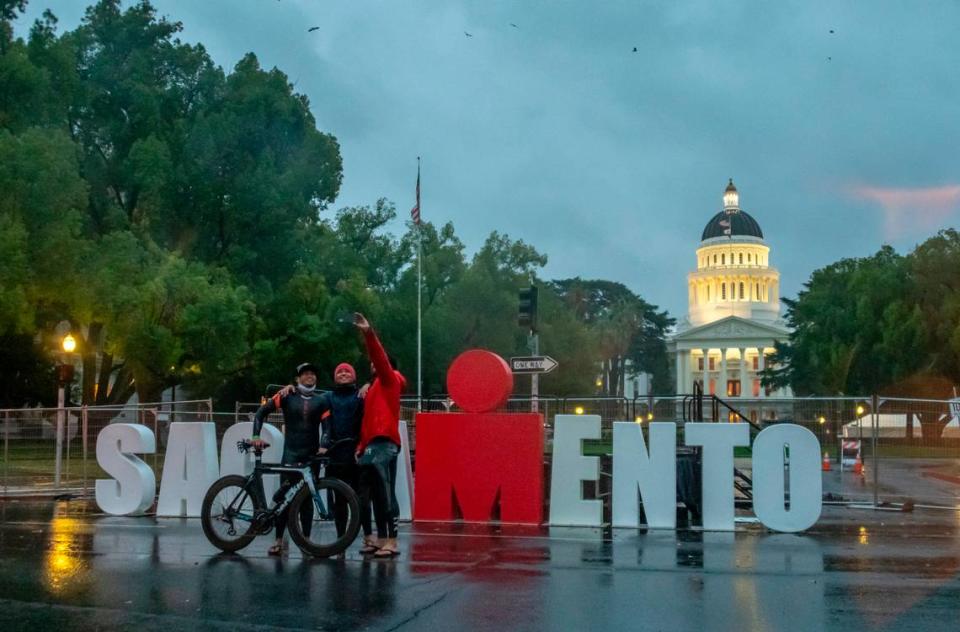 Orange County residents Raymond Soquena, Gary Binoya and Mike Sacramone, who had all planned to participate in the Ironman triathlon, take a selfie in front of the podium at the planned finish after the race was canceled because of weather on Sunday, Oct. 24, 2021.