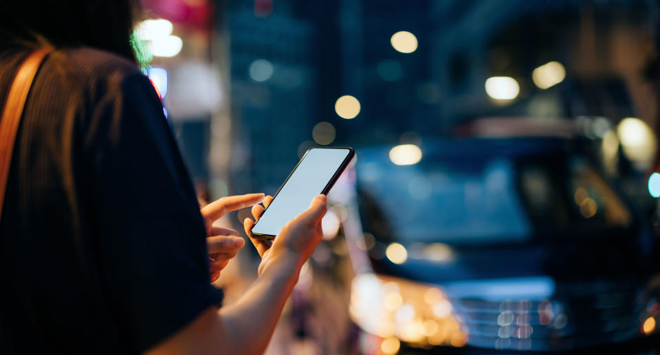Close up of young Asian woman using mobile app device on smartphone to hail a taxi ride on city street after work in the evening. Source: Getty Images