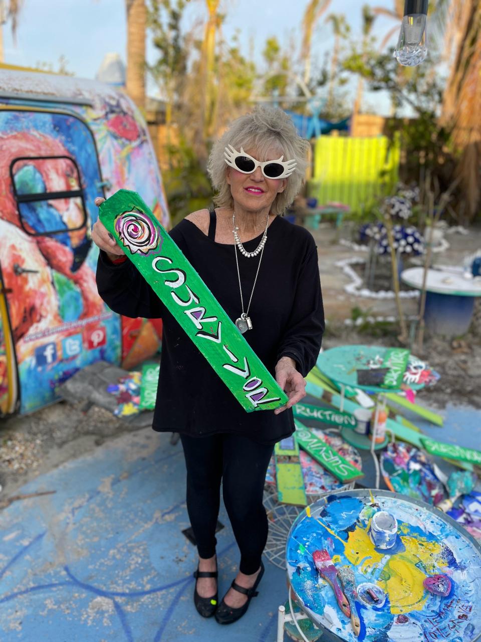 Artist Leoma Lovegrove poses with a painting made from a piece of fencing from her Hurricane Ian-damaged Matlacha gallery.