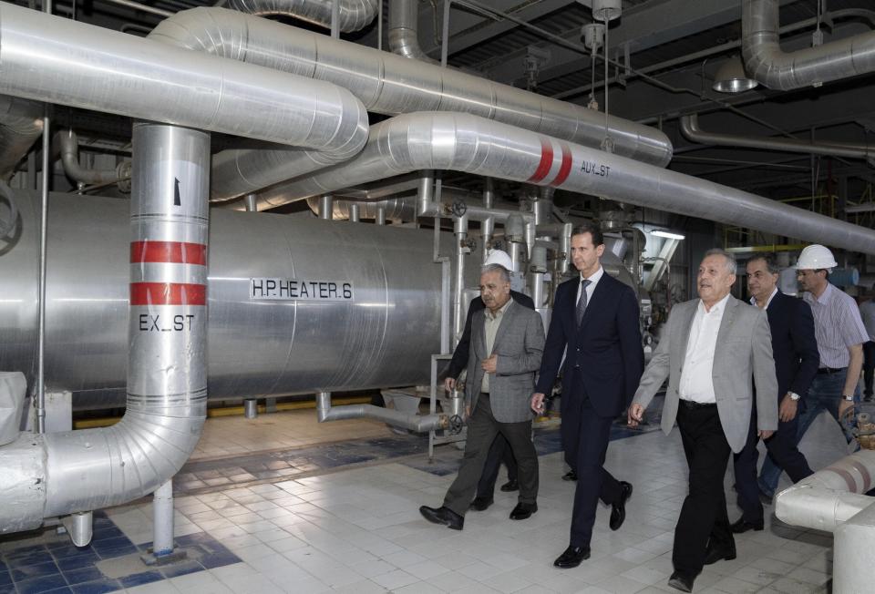 In this photo released on the official Facebook page of Syrian Presidency, Syrian President Bashar Assad, center, visits a power station in the eastern part of Aleppo province, Syria, Friday, July 8, 2022. Assad made a rare visit to the northern province of Aleppo on Friday to inaugurate a power station that was once held by insurgents and suffered wide damages during the war, state media reported. (Syrian Presidency Facebook page via AP)