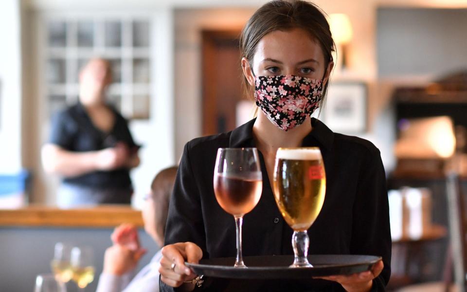 A staff member wears a face mask as she serves customers at the The Shy Horse pub and restaurant - Ben Stansall/AFP via Getty