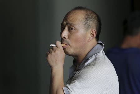 A man smokes a cigarette outside an office building in Beijing, China, May 29, 2015. REUTERS/Jason Lee