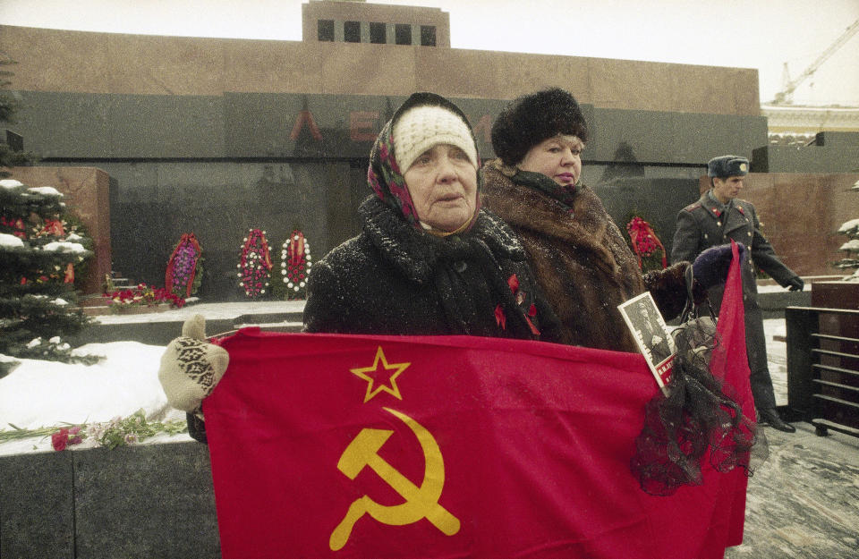 FILE - An elderly Communist supporter holds the flag of the former Soviet Union and a small portrait of Vladimir Lenin, the founder of the country, outside his mausoleum in Moscow's Red Square, Russia, on Jan. 21, 1994. On the 100th anniversary of his 1924 death, Lenin is still lauded by Communists, but he is more of an afterthought in modern Russia. (AP Photo/Alexander Zemlianichenko, File)