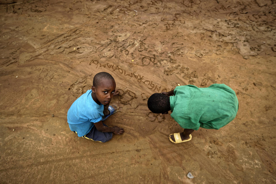 In this photo taken Thursday, April 4, 2019, the children of genocide survivors and perpetrators draw in the sand of their street following a rainstorm, in the reconciliation village of Mbyo, near Nyamata, in Rwanda. Twenty-five years after the genocide the country has six "reconciliation villages" where convicted perpetrators who have been released from prison after publicly apologizing for their crimes live side by side with genocide survivors who have professed forgiveness. (AP Photo/Ben Curtis)