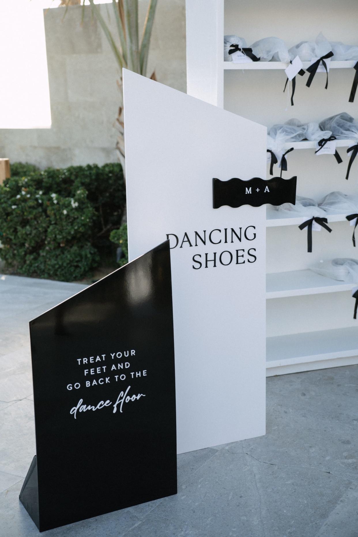 A black and white sign for "dancing shoes" sits in front of a shelf with bags of shoes on it. 