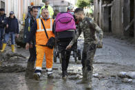 A rescuer helps a woman after heavy rainfall triggered landslides that collapsed buildings and left as many as 12 people missing, in Casamicciola, on the southern Italian island of Ischia, Sunday, Nov. 27, 2022. Firefighters are working on rescue efforts as reinforcements are being sent from nearby Naples, but are encountering difficulties in reaching the island either by motorboat or helicopter due to the weather. (AP Photo/Salvatore Laporta)