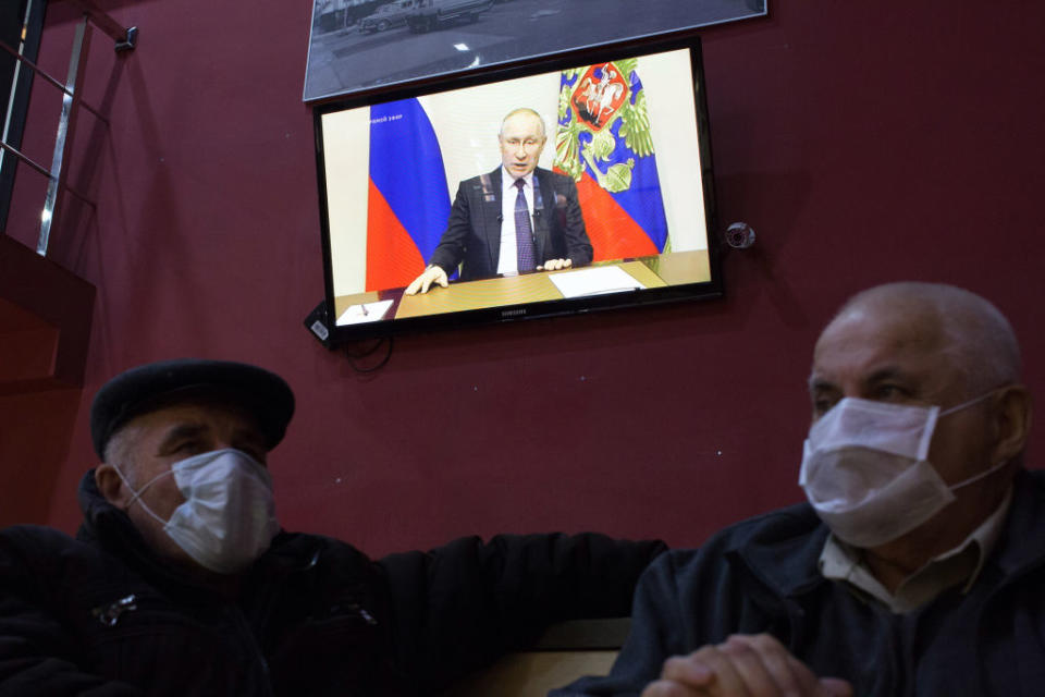 Customers wear protective face masks inside a cafe as a television screen displays Vladimir Putin, Russia's president, delivering a national address, in Moscow, Russia, on Wednesday, March 25, 2020. | Andrey Rudakov —Bloomberg via Getty Images