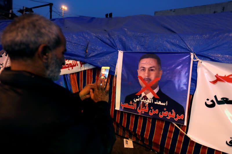 An Iraqi demonstrator takes a photo of a poster of Asaad al-Edani, Basra governor and a candidate for the prime minister office during ongoing anti-government protests in Baghdad