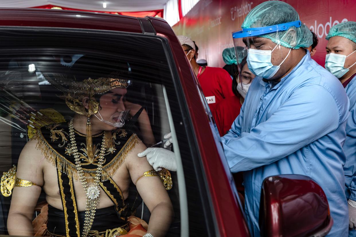 A man wearing a Javanese traditional costume receives a dose of the Sinovac Biotech Ltd. Covid-19 vaccine in a vehicle during a mass drive-thru vaccination program at the Prambanan temple complex on April 5, 2021, in Yogyakarta, Indonesia.