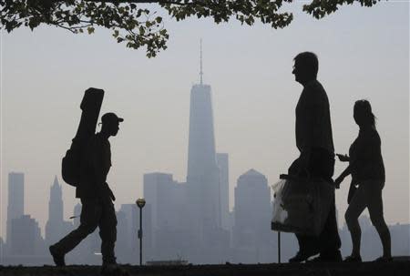 People walk past the skyline of New York's Lower Manhattan and One World Trade Center in a park along the Hudson River in Hoboken, New Jersey, September 11, 2013. REUTERS/Gary Hershorn