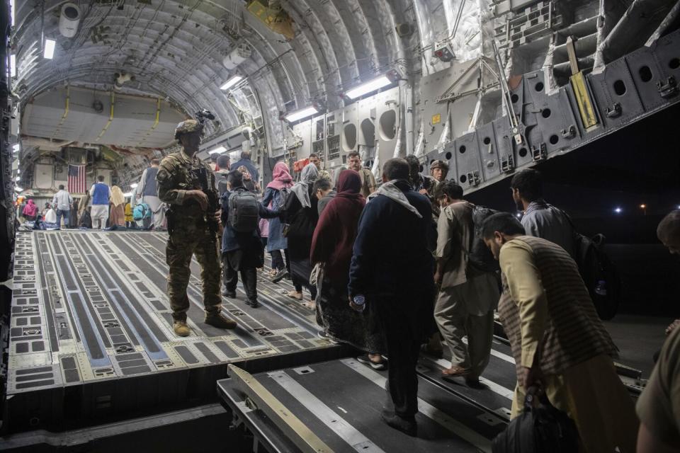 A man in military fatigues, left, stands watching a line of people entering a cavernous military aircraft