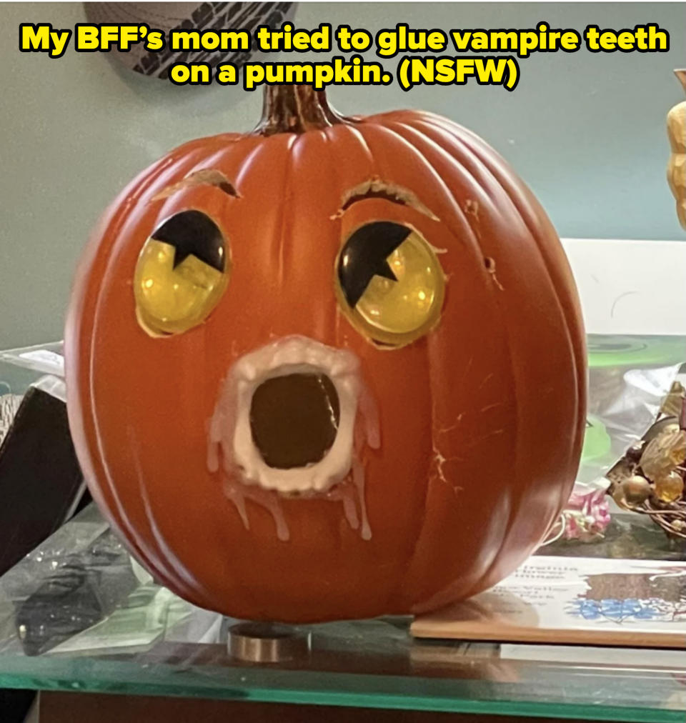 A carved pumpkin with wide, surprised eyes and a dripping, open mouth displayed on a glass shelf