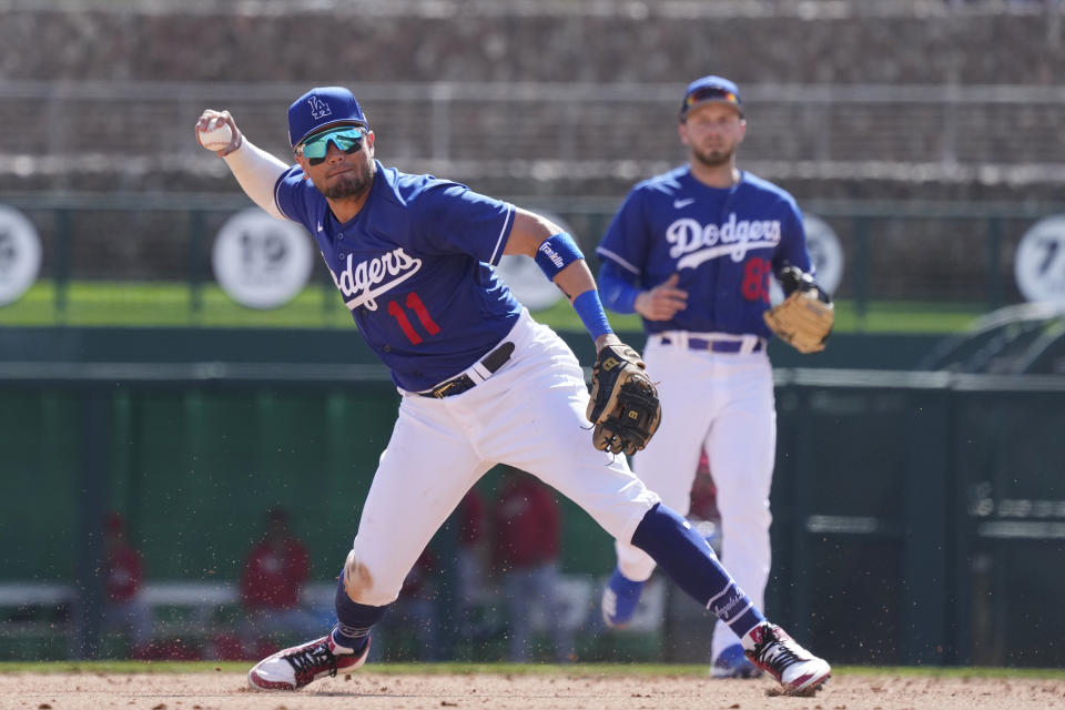 Los Angeles Dodgers shortstop Miguel Rojas (11) makes a late throw to third base as Dodgers second baseman Michael Busch (83) looks on during the fifth inning of a spring training baseball game against the Cincinnati Reds Tuesday, Feb. 28, 2023, in Phoenix. (AP Photo/Ross D. Franklin)