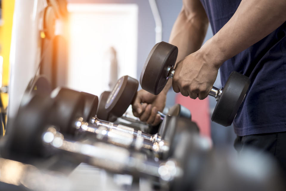 A person is lifting a dumbbell in a gym, focusing on their workout. Several other dumbbells are lined up in the foreground.